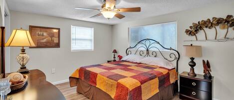 A bedroom with a bed, a nightstand, a desk, and a ceiling fan.