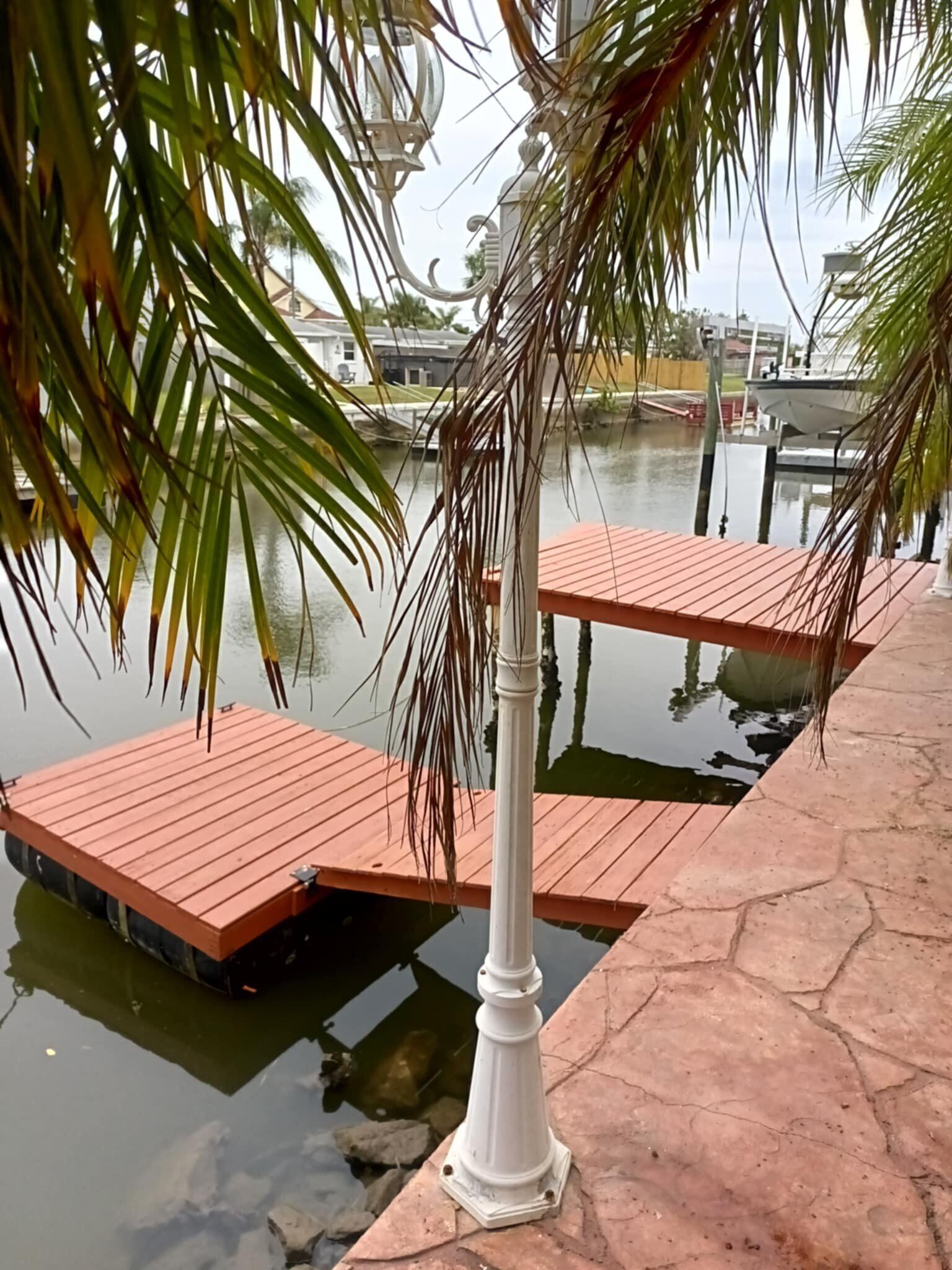 A wooden dock extending into a body of water, surrounded by palm trees and a white lamp post.