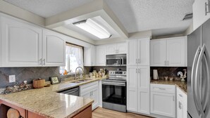Una cucina moderna con mobili bianchi, elettrodomestici in acciaio inossidabile, un piano di lavoro in granito e un forno integrato.
