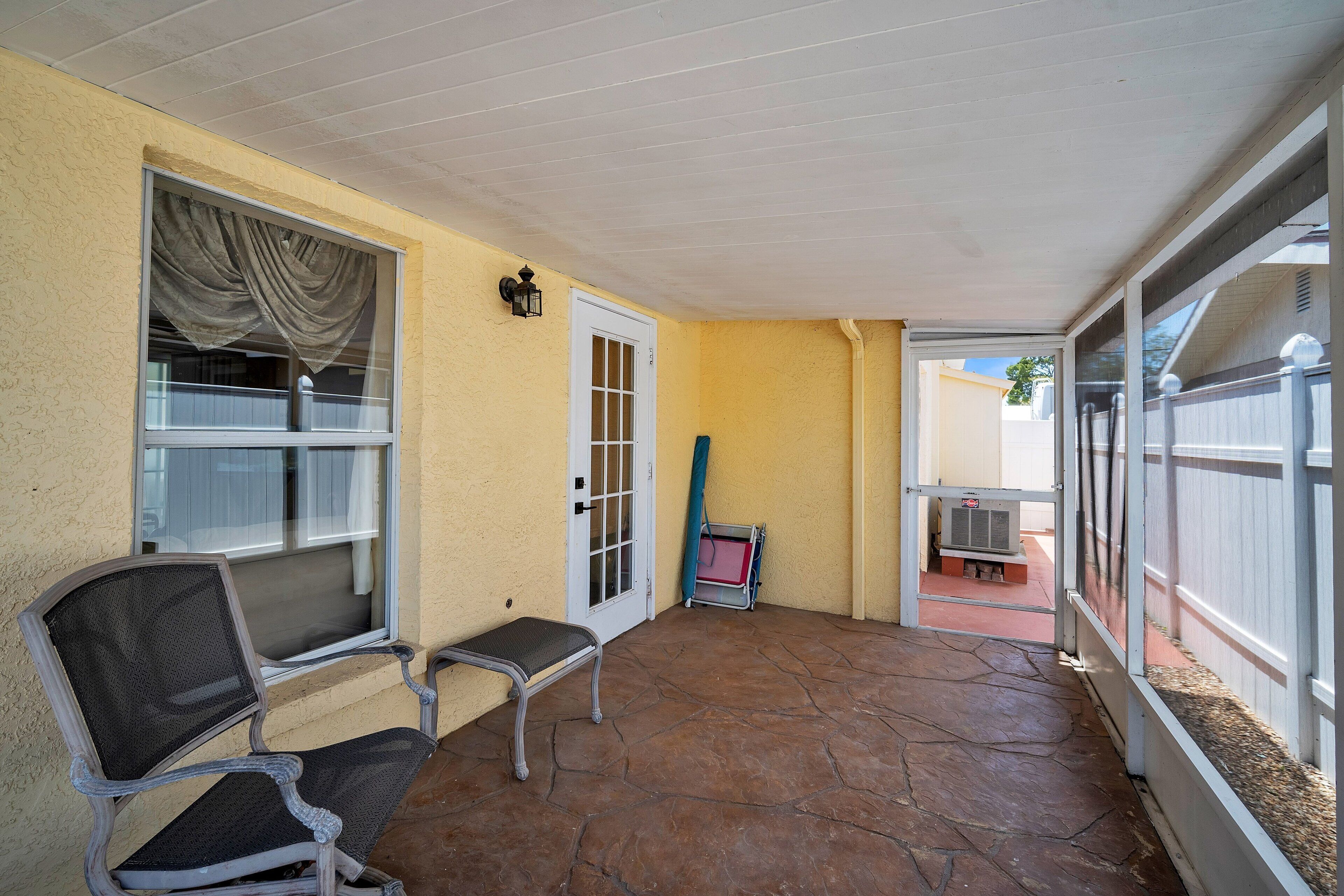Un espacio cubierto con patio, un banco, una puerta y vista al jardín trasero.