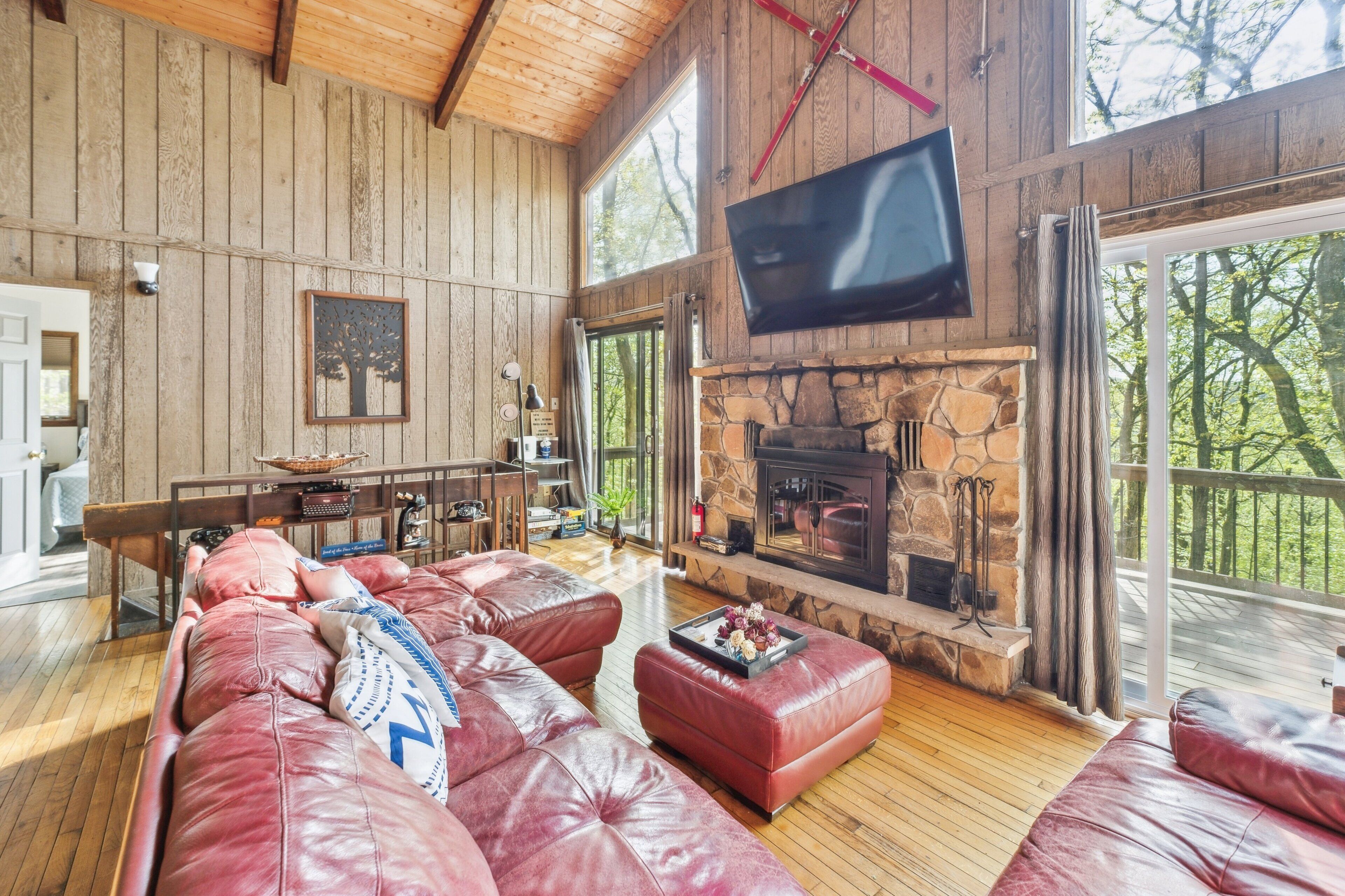 A spacious living room with a stone fireplace, leather sofas, and a large TV mounted on the wall.