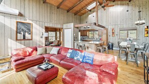 A spacious living room with a red leather sectional sofa, a wooden ceiling, and a kitchen area visible through an open doorway. - Charming Porter House In The Heart Of The Poconos 4 Bedroom Chalet (Bushkill)