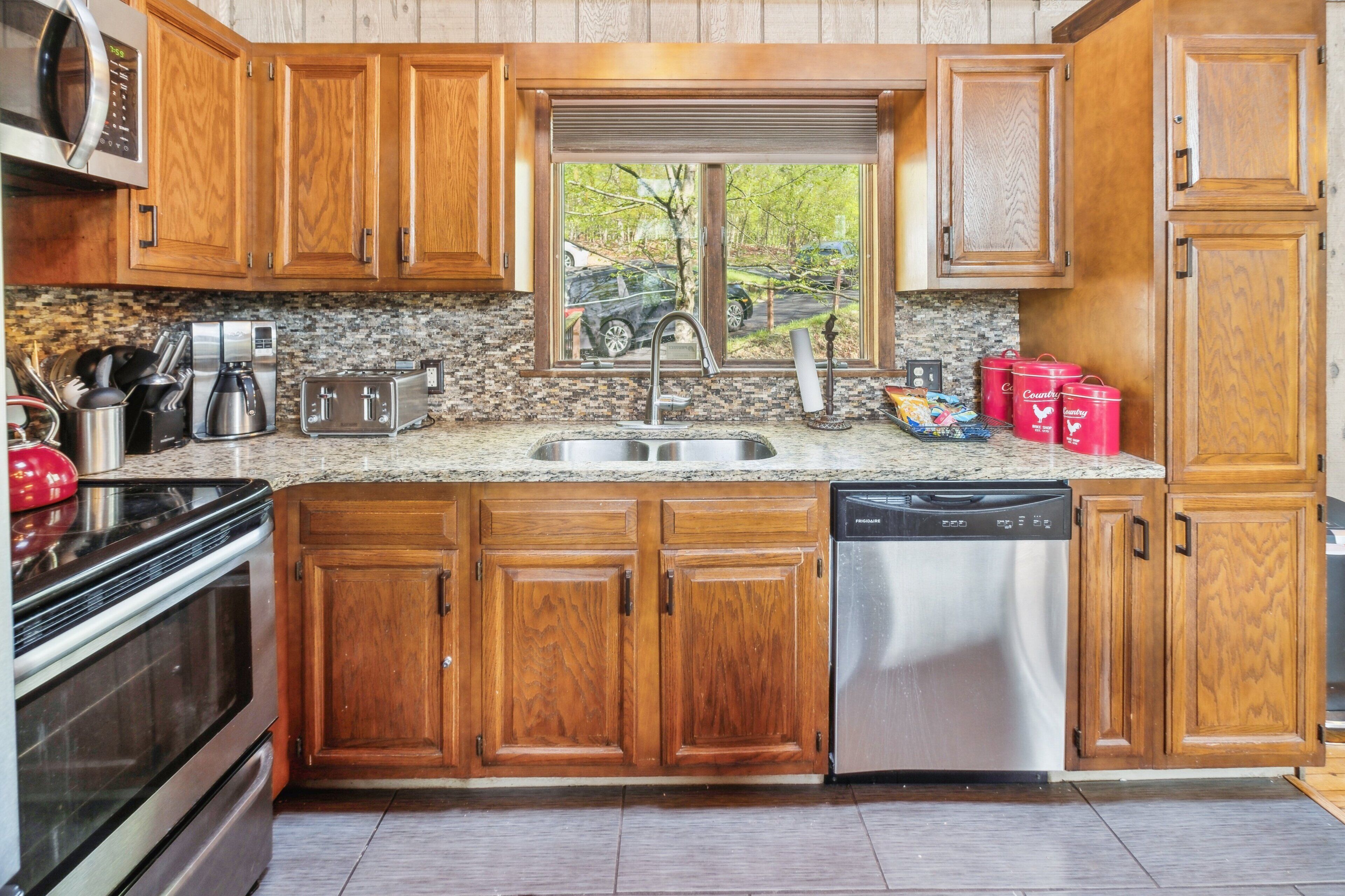 Una cocina con armarios de madera, encimera de granito, pileta de acero inoxidable, lavavajillas y ventana con vista al exterior.