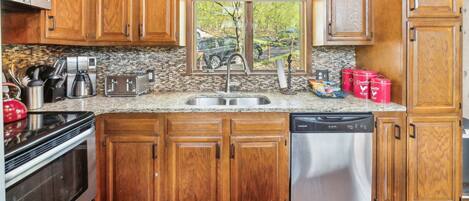 Una cocina con armarios de madera, encimera de granito, pileta de acero inoxidable, lavavajillas y ventana con vista al exterior.
