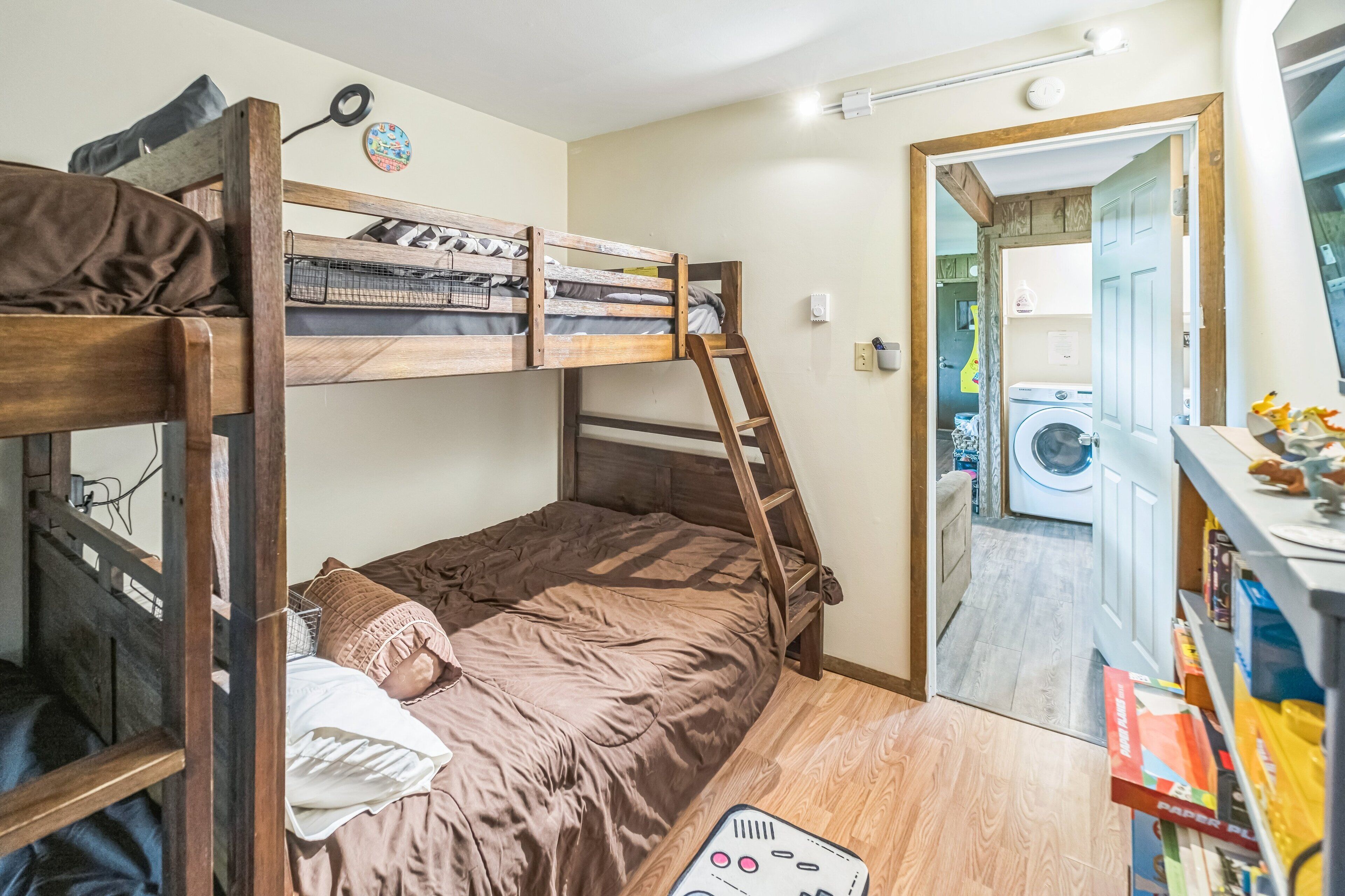 A bunk bed room with a ladder, a washing machine, and a shelf with toys.