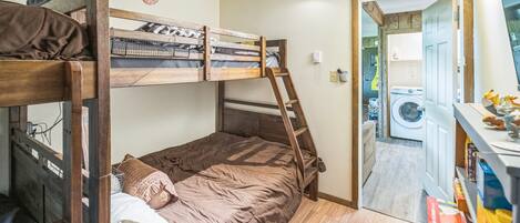 A bunk bed room with a ladder, a washing machine, and a shelf with toys.