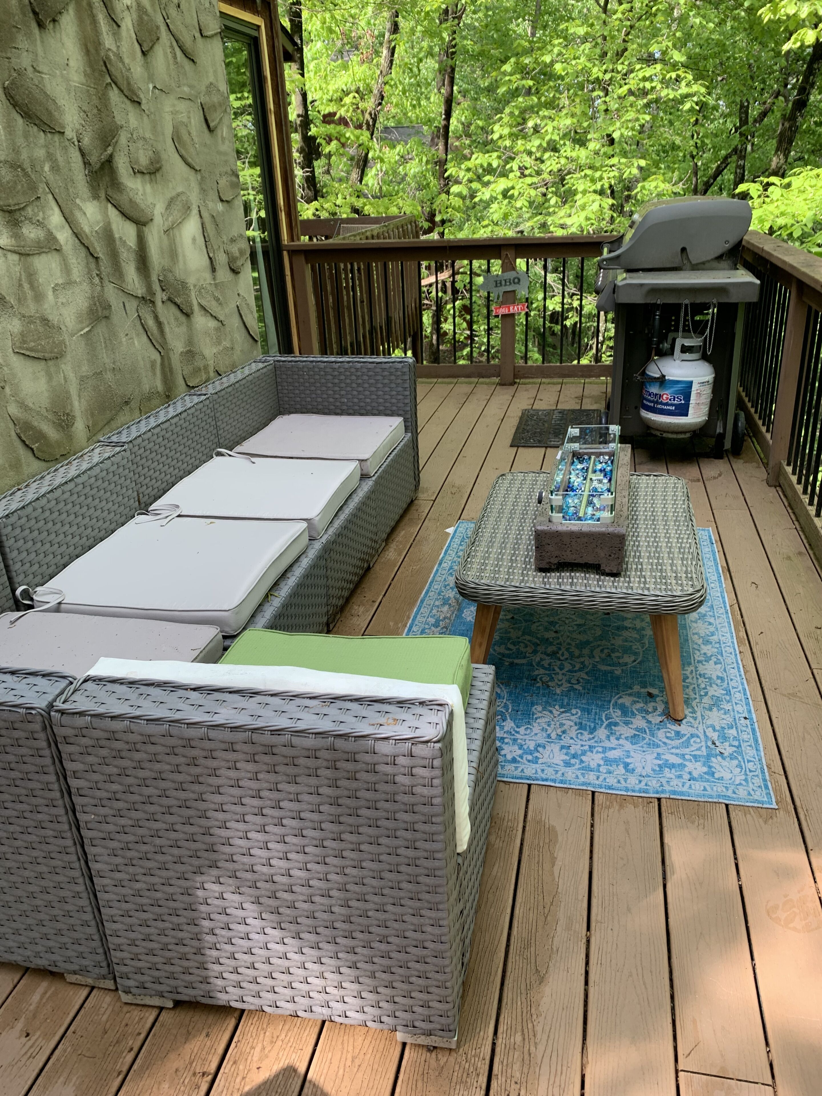 Une terrasse couverte, aménagée avec des meubles en osier, un barbecue et une bouteille de propane.