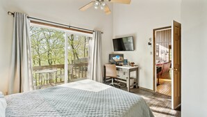 A bedroom with a large bed, a desk, a TV, and a balcony with a view of trees. - Charming Porter House In The Heart Of The Poconos 4 Bedroom Chalet (Bushkill)