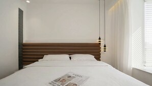 A neatly made bed with a magazine on it, a wooden headboard, and a hanging light fixture.