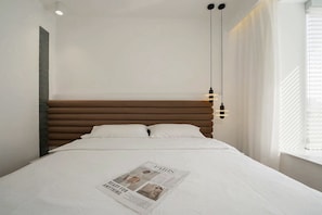 Relax in a serene bedroom with a low-profile headboard, white bedspread, and a reading spot.