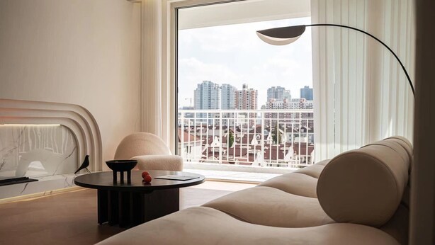 A modern living room with a sofa, a round coffee table, and a view of a cityscape through large windows.