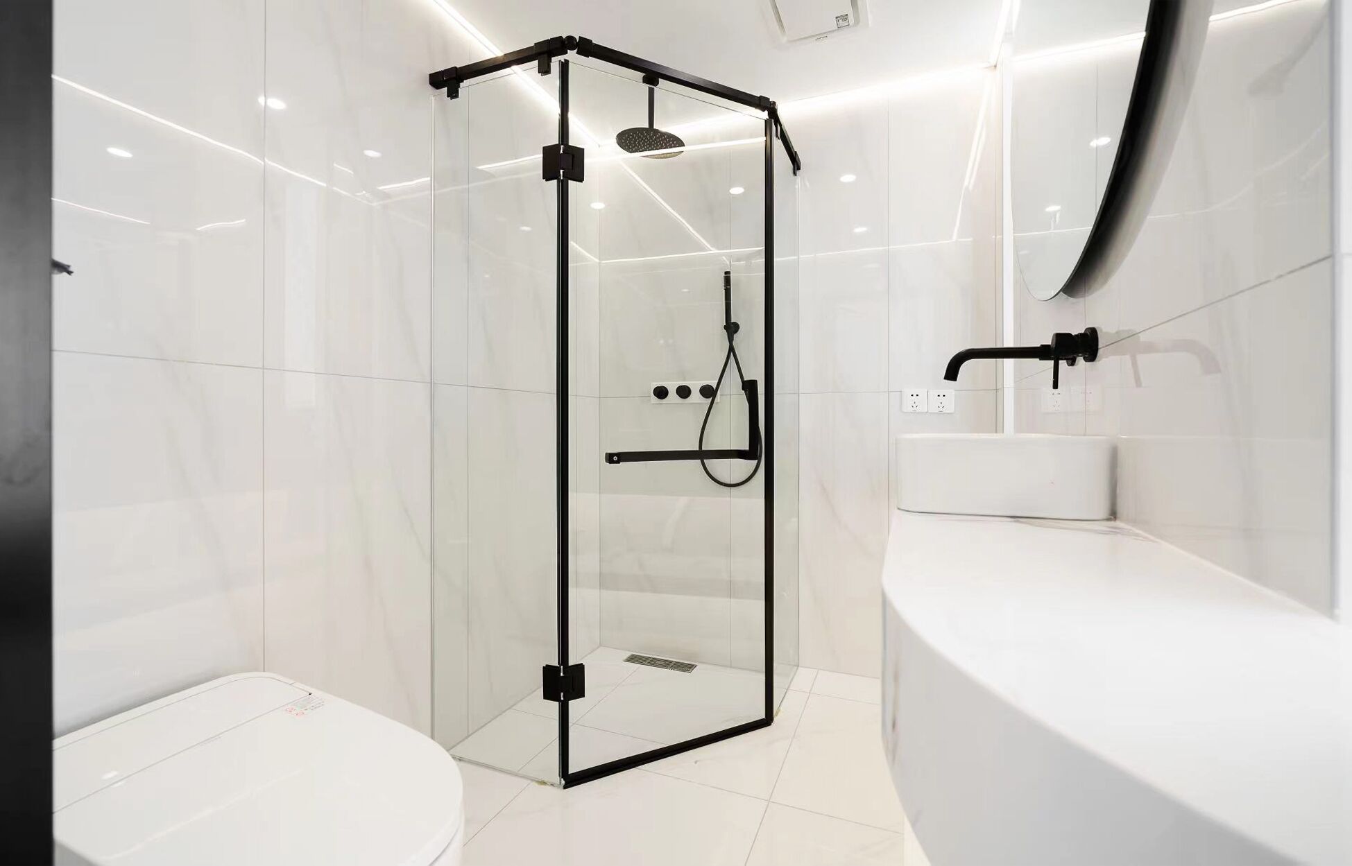 Un baño moderno con ducha de mampara de vidrio, lavabo blanco y espejo grande.