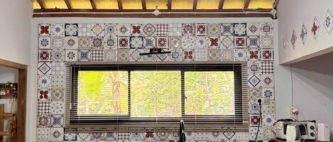 A kitchen with a wooden ceiling, a tiled backsplash, a window with blinds, and a wooden countertop.
