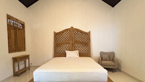 A bedroom with a wooden bed frame, a nightstand, a chair, and a decorative wooden panel on the wall. - Omah Ndoro Sugih (Triwidadi)