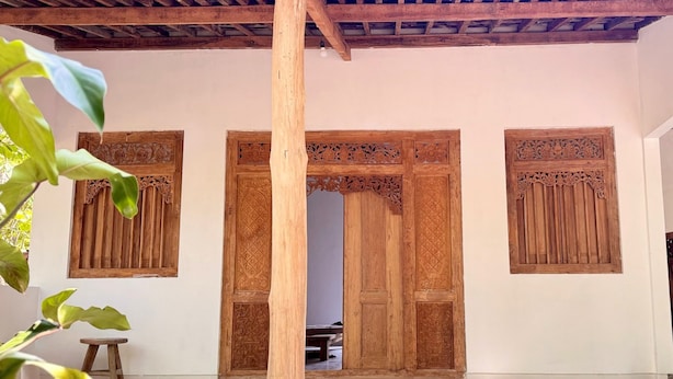 A traditional wooden door with intricate carvings, a tiled floor, and a wooden ceiling structure. - Omah Ndoro Sugih (Triwidadi)