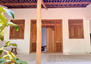 A traditional wooden door with intricate carvings, a tiled floor, and a wooden ceiling structure.