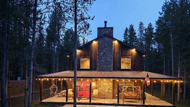 Ein zweistöckiges Holzhaus mit einem Steinkamin, einer überdachten Veranda mit Lichterketten und einer roten Tür.