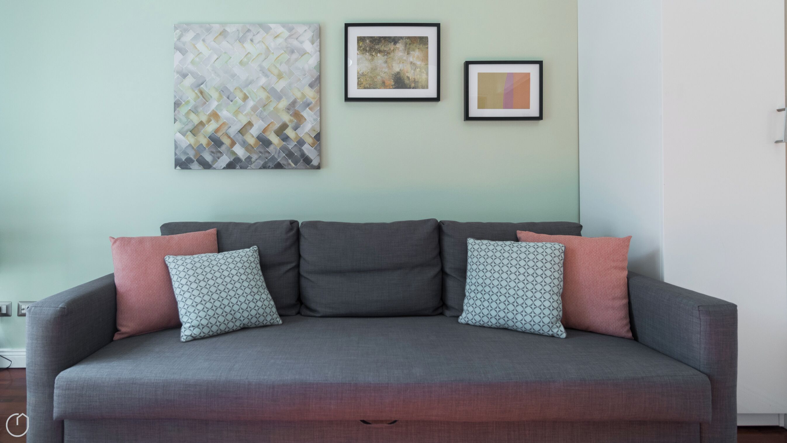 A grey sofa with patterned cushions against a light green wall, flanked by abstract art pieces.