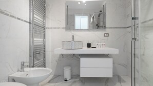 Un bagno moderno con bidet, WC, lavandino con specchio sopra e zona doccia.