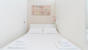 Un letto rifatto con lenzuola bianche, una lampada a parete e un elemento decorativo a muro.