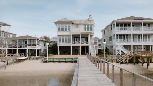 A beachfront property with a wooden boardwalk leading to a multi-story building with balconies. - The Seafarer (Wrightsville Beach)