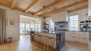 A modern kitchen with a marble island, wooden bar stools, and a view of the city. - The Seafarer (Wrightsville Beach)