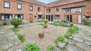 A courtyard with a gravel path, surrounded by brick buildings with multiple windows and doors. - Host Stay West Barn (Fakenham)