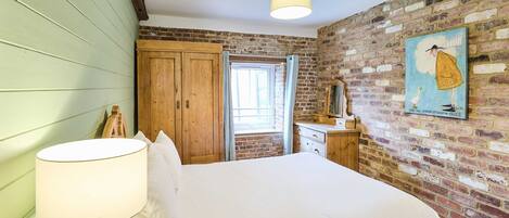 Ein Schlafzimmer mit einem Bett, einem Holzschrank, einer Kommode, einer Lampe und einem Bild an der Wand.