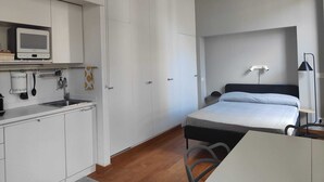 A compact room with a bed, a small desk, a kitchenette with a microwave, and a ceiling-mounted TV. - Citrus Pop Holiday home in Piazza del Popolo (Roma)