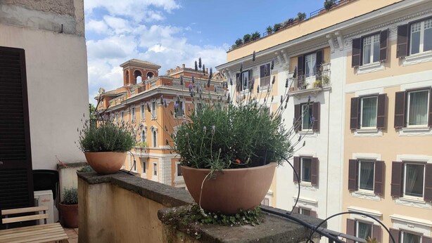 A balcony with terracotta planters, a wooden bench, and a view of historic buildings. - Citrus Pop Holiday home in Piazza del Popolo (Roma)