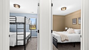 A room with bunk beds, a window with a view, a bed with a lamp, and artwork on the wall. - Northern Comfort: The Vault - Your Refined Retreat near Duluth (Hermantown)