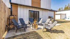 A modern outdoor patio with Adirondack chairs, a fire pit, and a grill. - Northern Comfort: The Vault - Your Refined Retreat near Duluth (Hermantown)