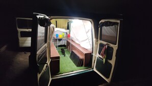 A van with an open door revealing a small, compact living space with a bed, a table, and a green mat. - Vintage Camper Van in Mallorca, with everything for live, 9 persons driving. (Sol de Mallorca)