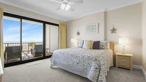 A bedroom with a bed, a nightstand, a lamp, a ceiling fan, a window with curtains, and a balcony with chairs. - Grand Pointe 310, panoramic views, huge balcony, 3rd floor with 3 bedrooms, 3.5 baths (Orange Beach)
