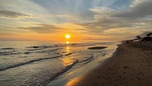 A beach with the sun setting over the horizon, calm waves, and a few people walking along the shore. - Al Fattah Luxury (Estepona)