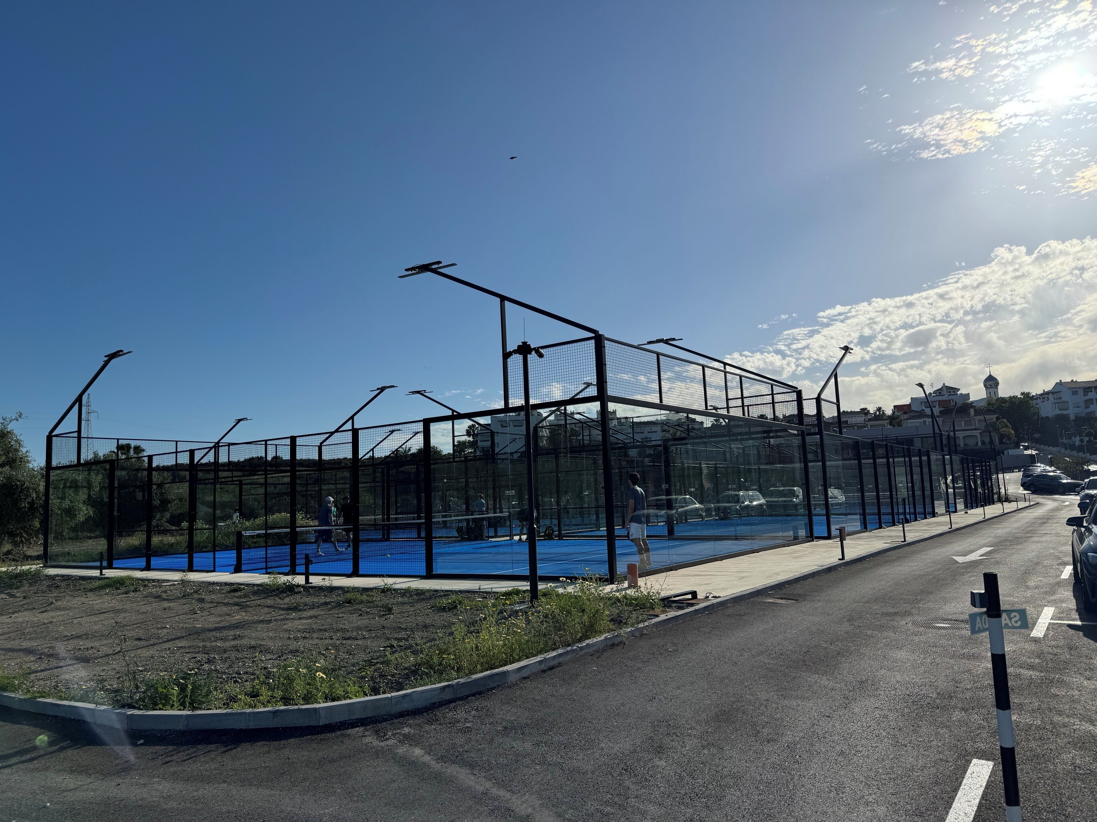 A tennis court with a net, surrounded by a fence, and a road with cars passing by.