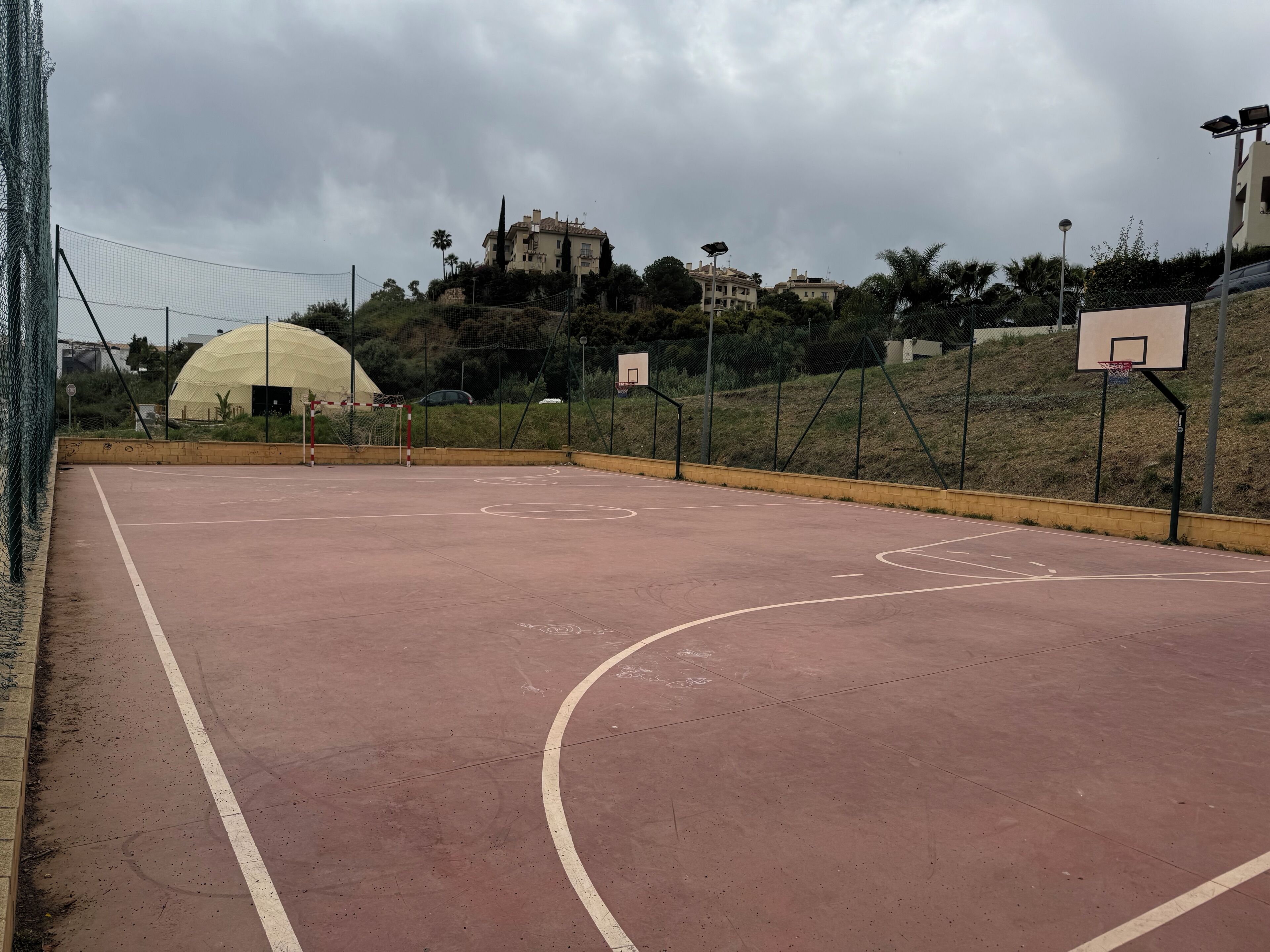 An outdoor basketball court with a net, a hoop, and a dome structure in the background.