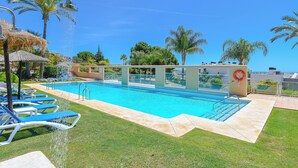A swimming pool with clear blue water, surrounded by grass and palm trees. - Al Fattah Luxury (Estepona)