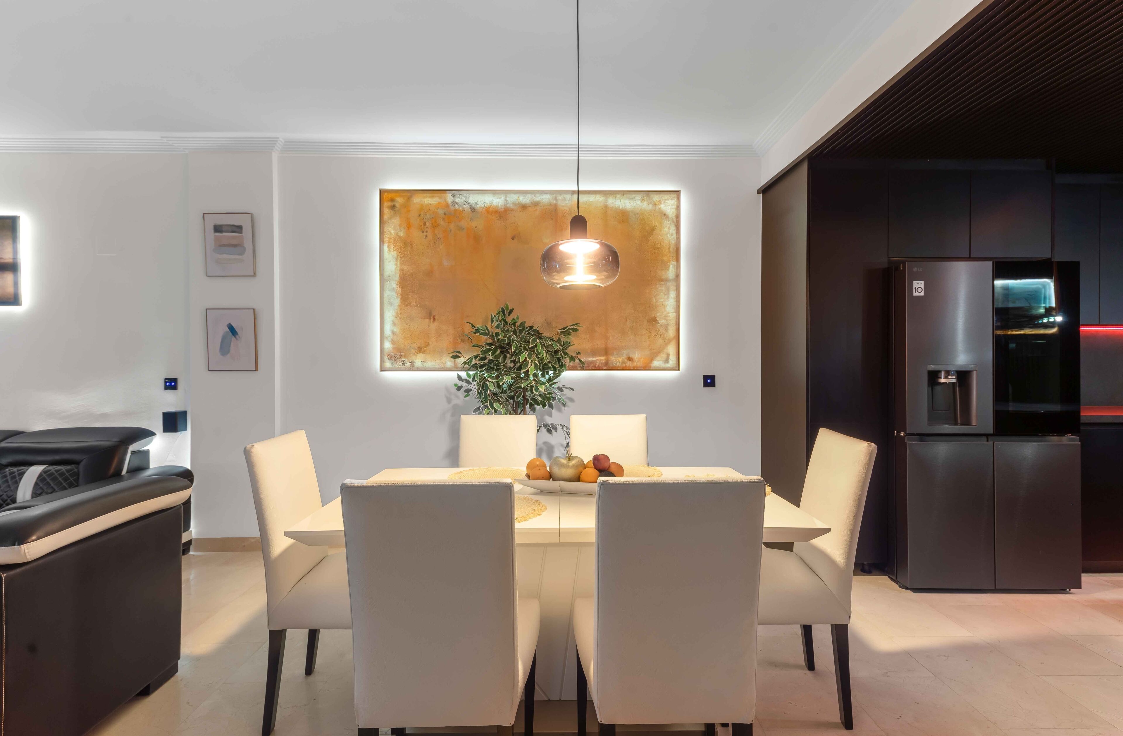 Un espace repas moderne comprenant une table, des chaises, un luminaire suspendu, une plante et un réfrigérateur.