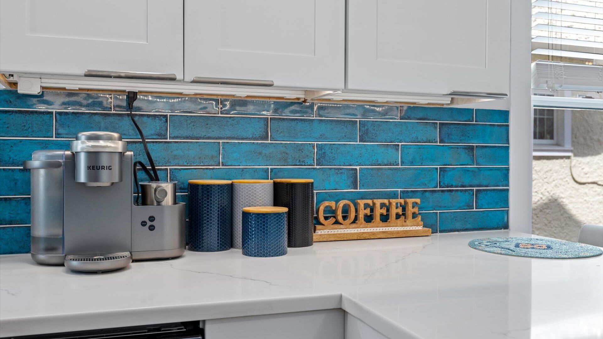 A kitchen counter with a coffee maker, a kettle, and a coffee-themed decorative piece.