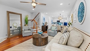 A spacious living room with a wooden staircase, a dining area, and a kitchen in the background.