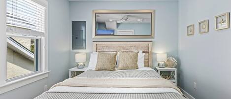 Une chambre avec un grand lit, deux tables de chevet, un ventilateur de plafond et une fenêtre avec des stores.