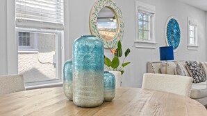 A room with a round wooden table, large vases, a mirror, and a view of a beach through the window.
