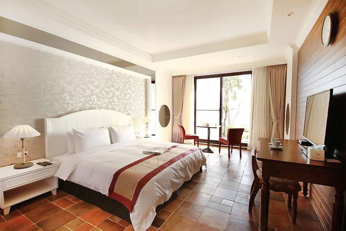 A hotel room with a large bed, a desk with a chair, a TV, and a window with curtains.