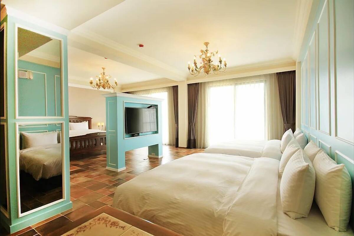 A hotel room with a large bed, a television, a mirror, and a chandelier.