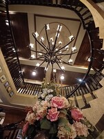 Una imponente escalera con un candelabro y un arreglo floral en la parte superior.