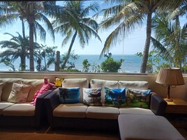 Una sala de estar con un sofá orientado hacia una ventana con vista al mar, decorada con varios cojines y una lámpara.