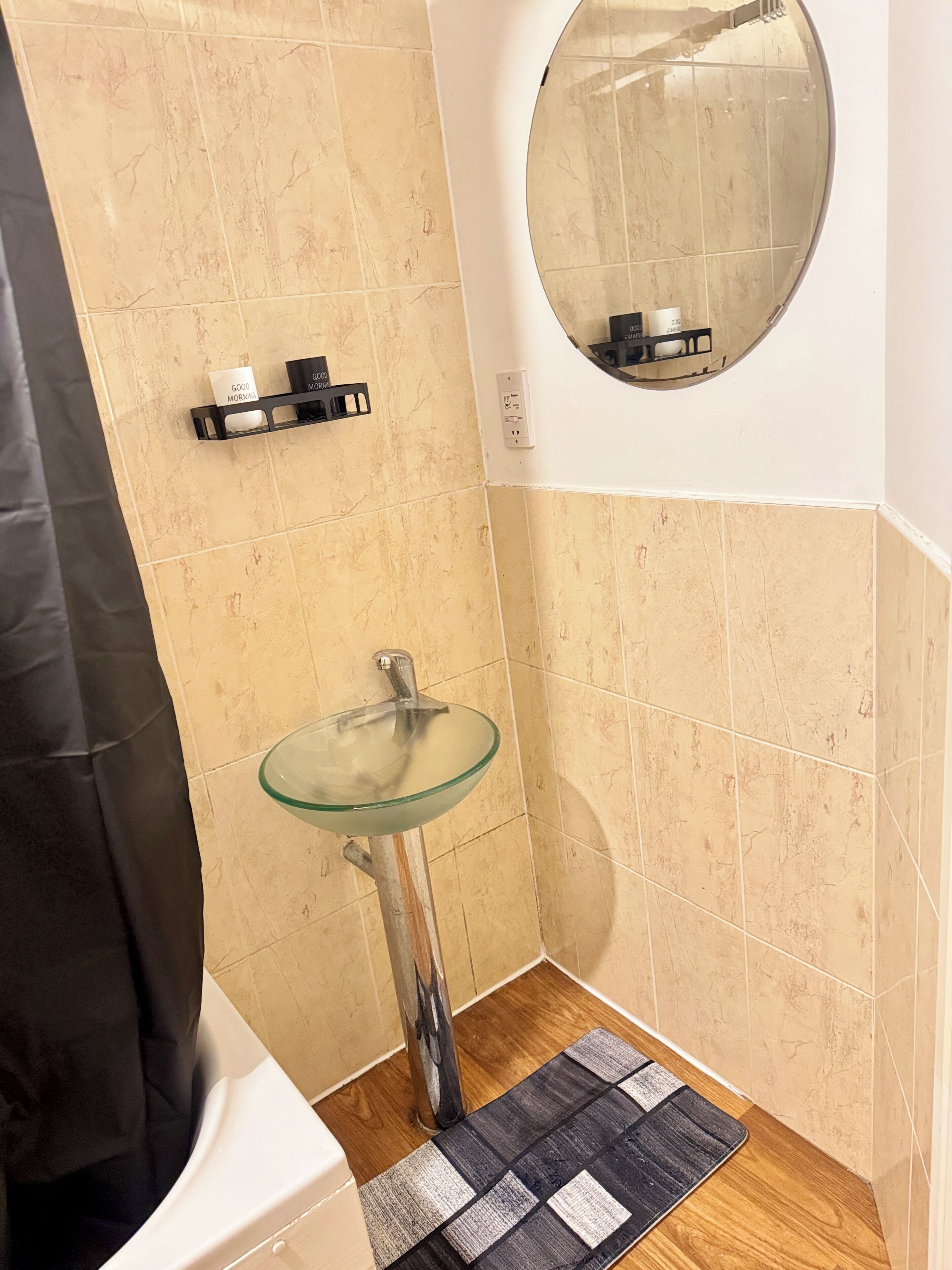 A bathroom with a glass sink, beige tiles, a black towel rack, and a mirror.