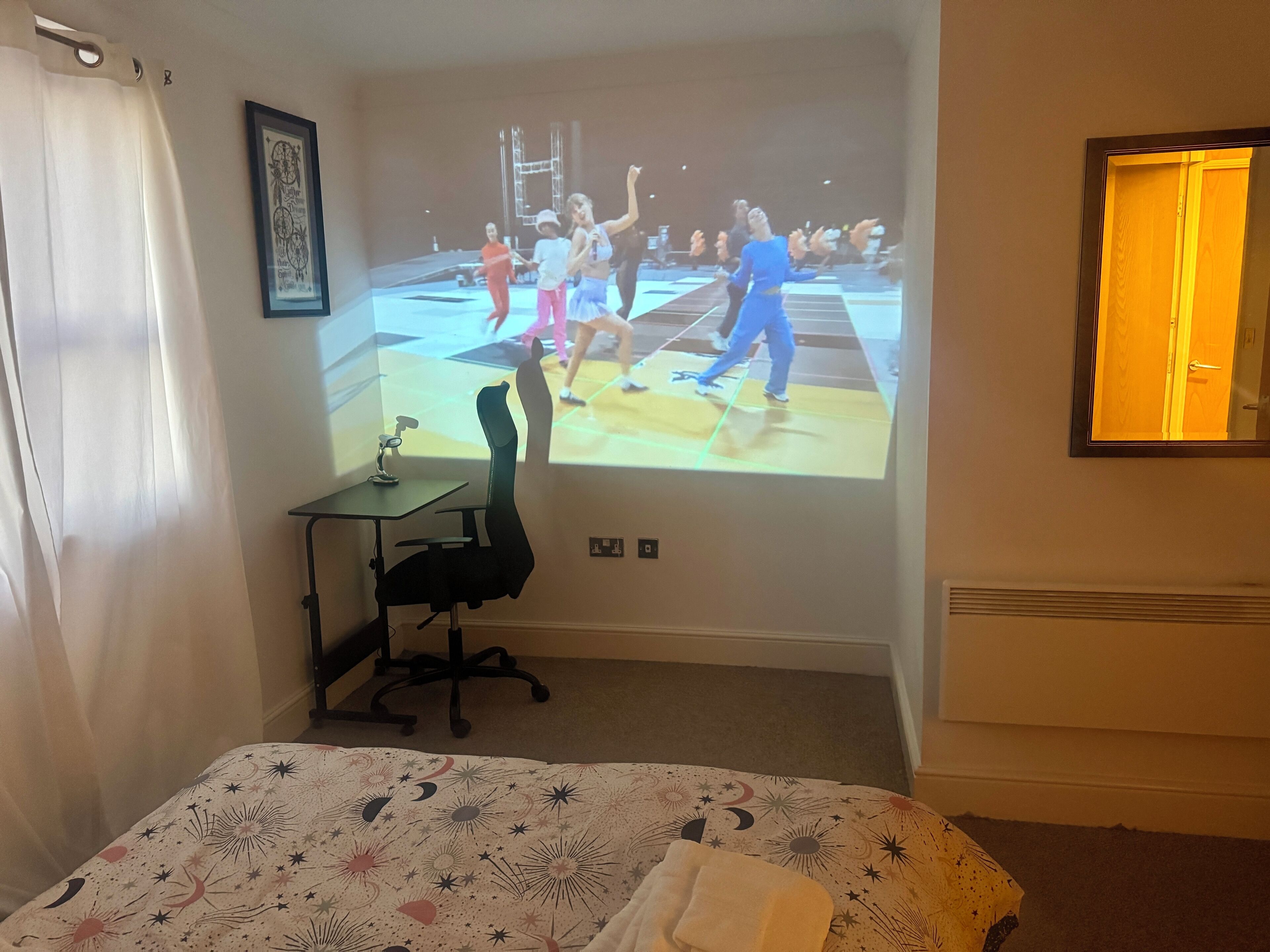 Ein Hotelzimmer mit einem Bett, einem Schreibtisch und einem großen Bildschirm, der ein Basketballspiel zeigt.