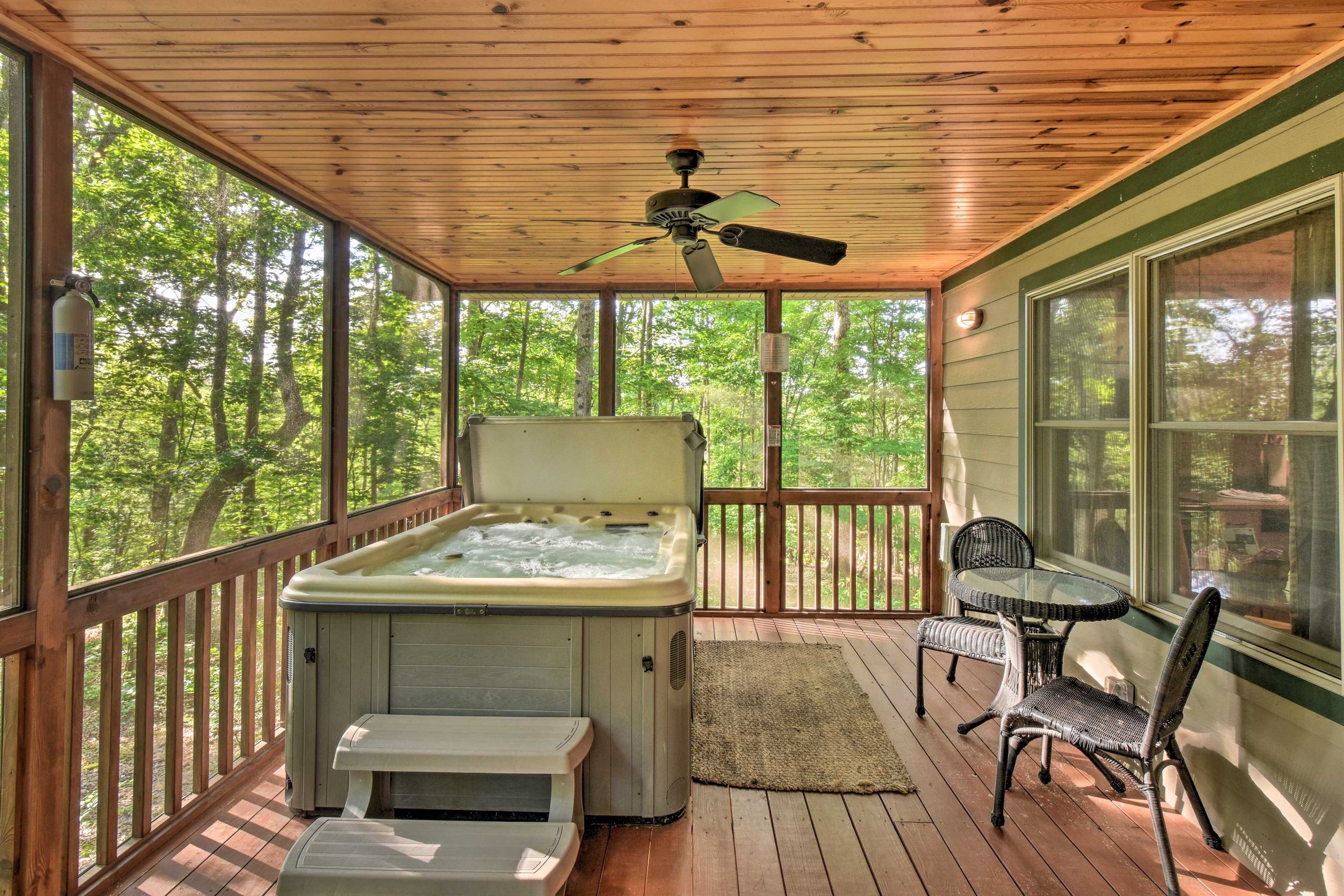 Una terraza de madera con un jacuzzi, un ventilador de techo y una mesa con sillas.